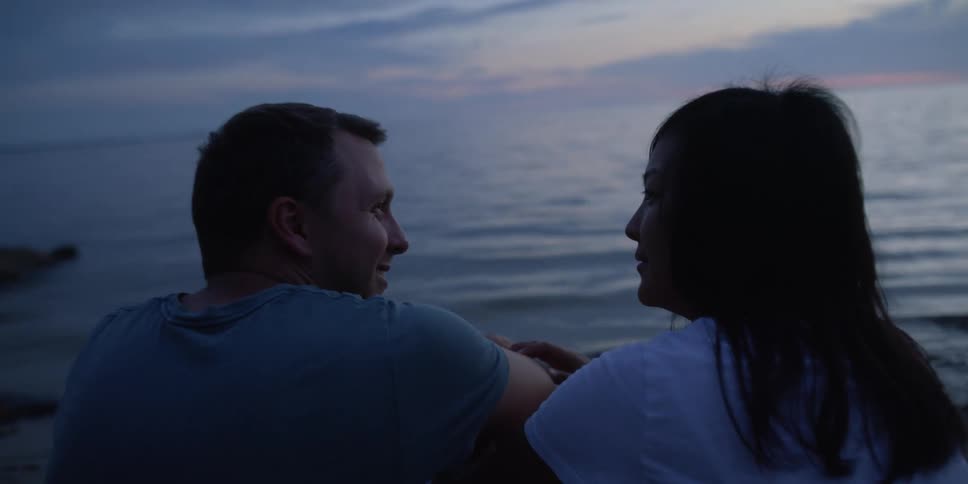 A man and woman talking with each other outdoors near the edge of some water