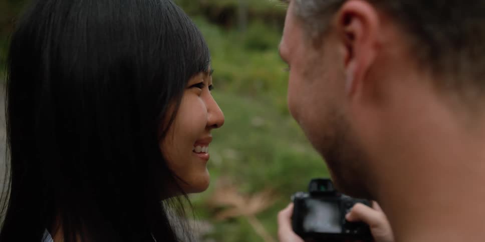 A man and a woman look at a camera screen while standing next to one another outdoors