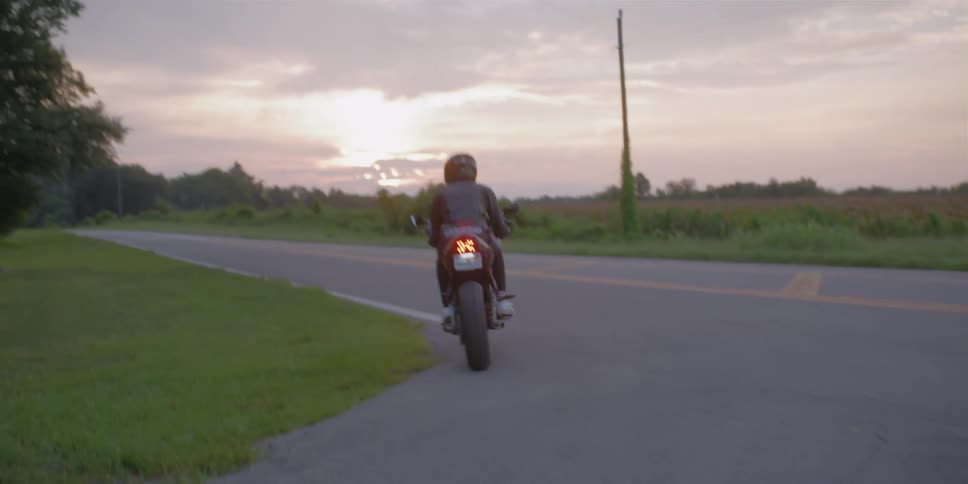 A man is driving a motorcycle in a rural area at dusk