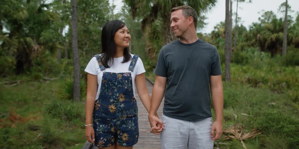 A man and woman stand on a path in a garden and hold hands and smile at one another