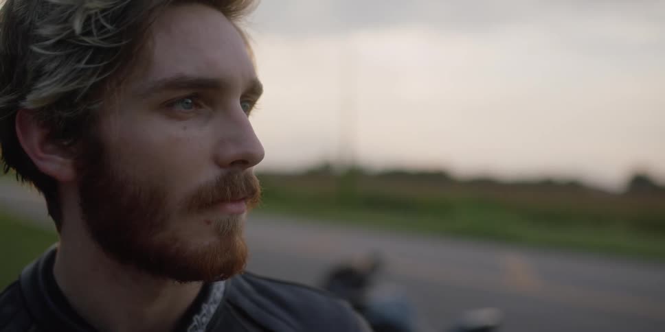 Young bearded man standing near a motorcycle in a road in the countryside