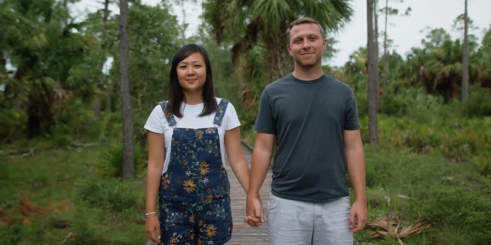 A couple holds hands as they stand on a pier surrounded with palm trees