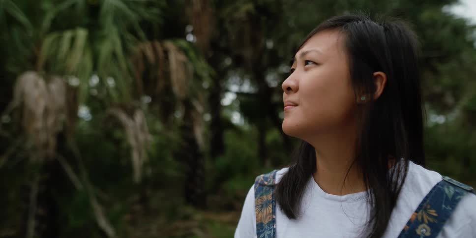 Young asian woman looking up near a tropical forest