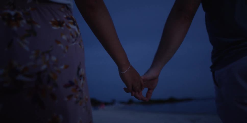 Man and woman holds hands as they walk on the beach