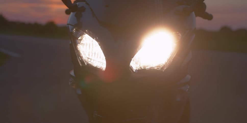 Man turns on the motorcycle headlights on the highway at dusk