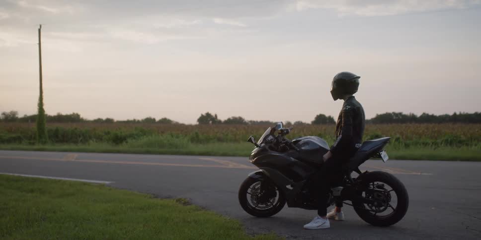 A motorcyclist sits on his bike while parked on the side of a rural highway