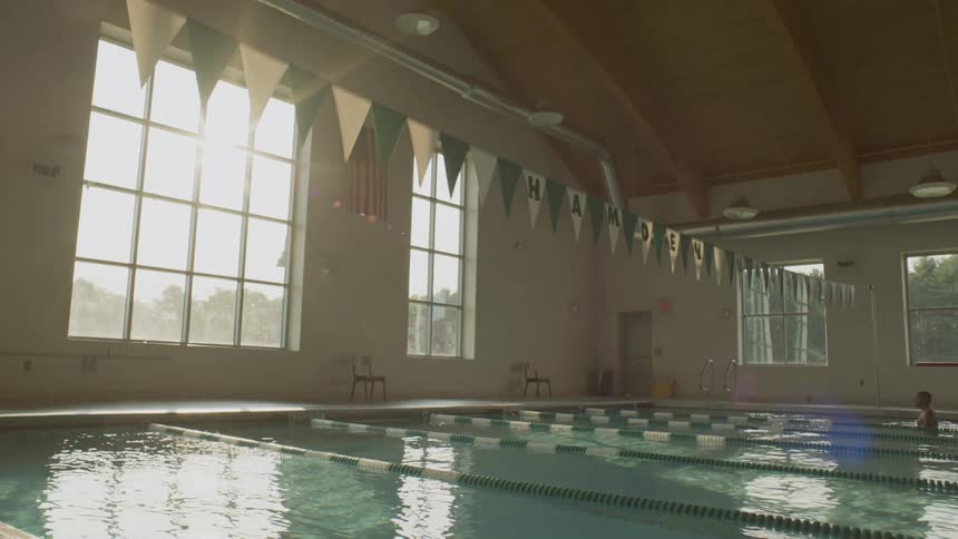 A man standing in an indoor pool that has racing lanes