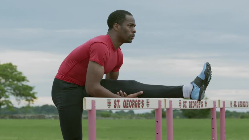 A man resting his leg on a hurdle as he stretches out on a cloudy day