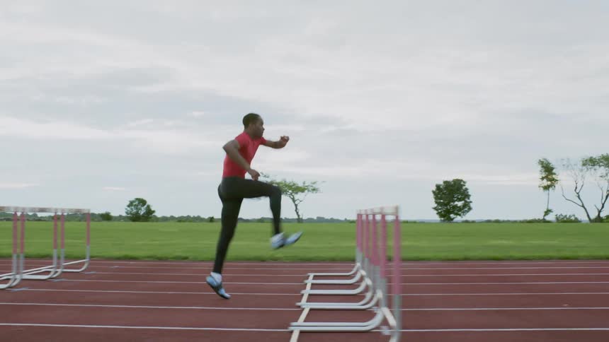 A runner is racing down a track jumping hurdles on a cloudy day