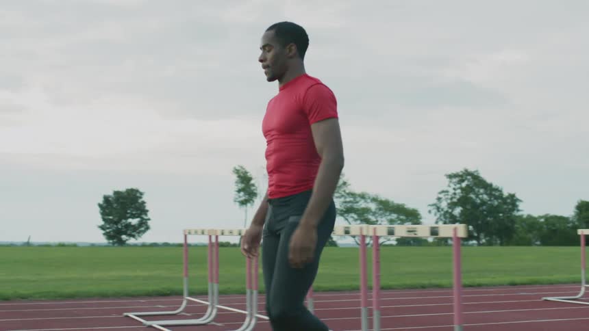 A man in athletic apparel walks past a series of hurdles on a track