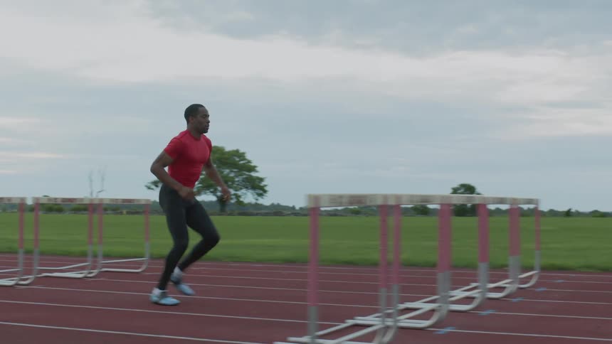 A man running and jumping hurdles on a cloudy day
