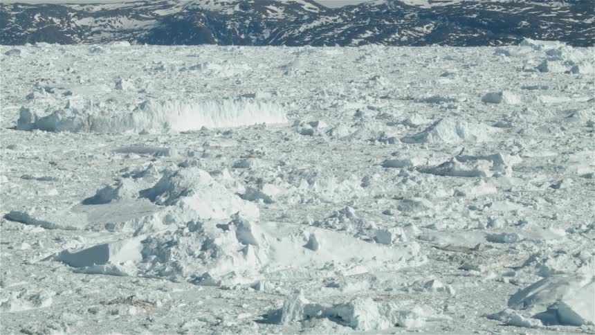 A glacier on a sunny day with mountains in the background