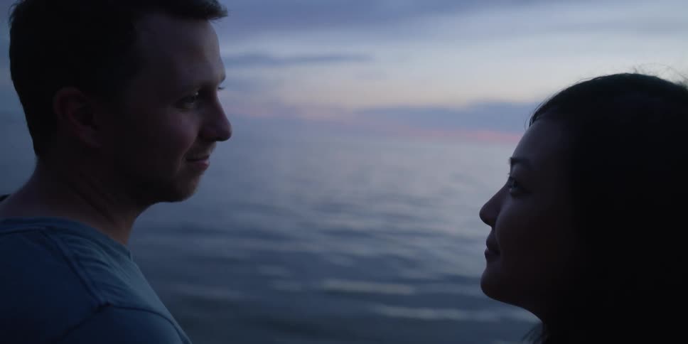 A man and woman are looking at each other by the ocean