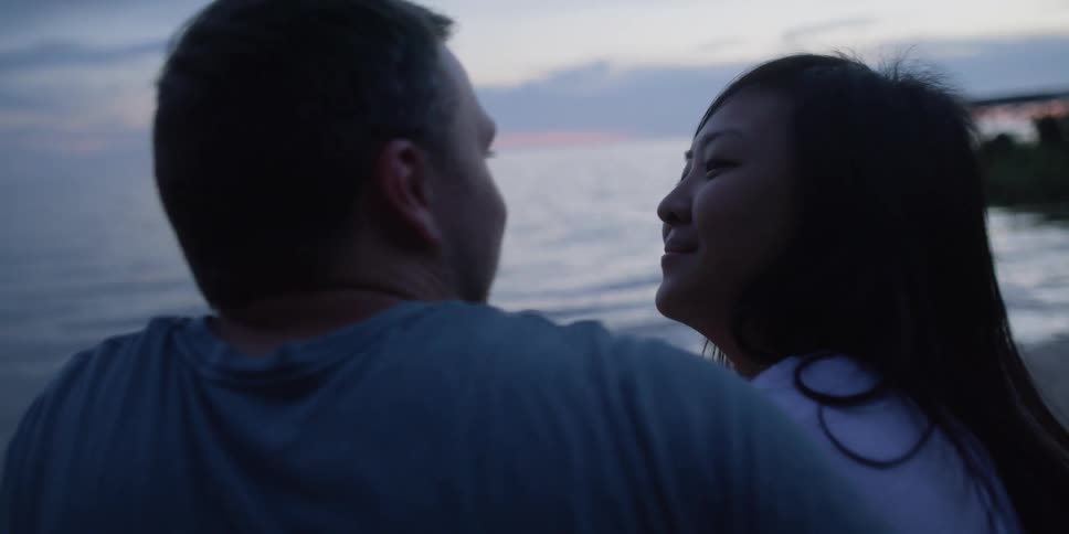 A man and woman sit together and cuddle on a quiet beach