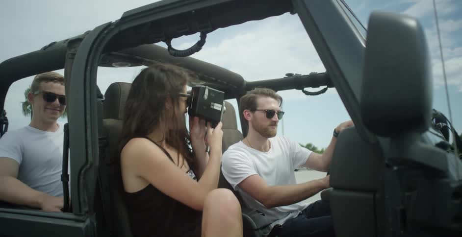 A woman films a man in a jeep