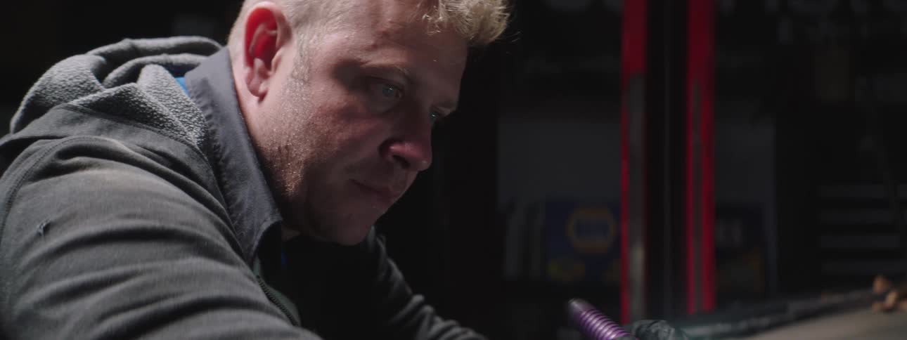 A man holds a tool in his hand as he works in a garage