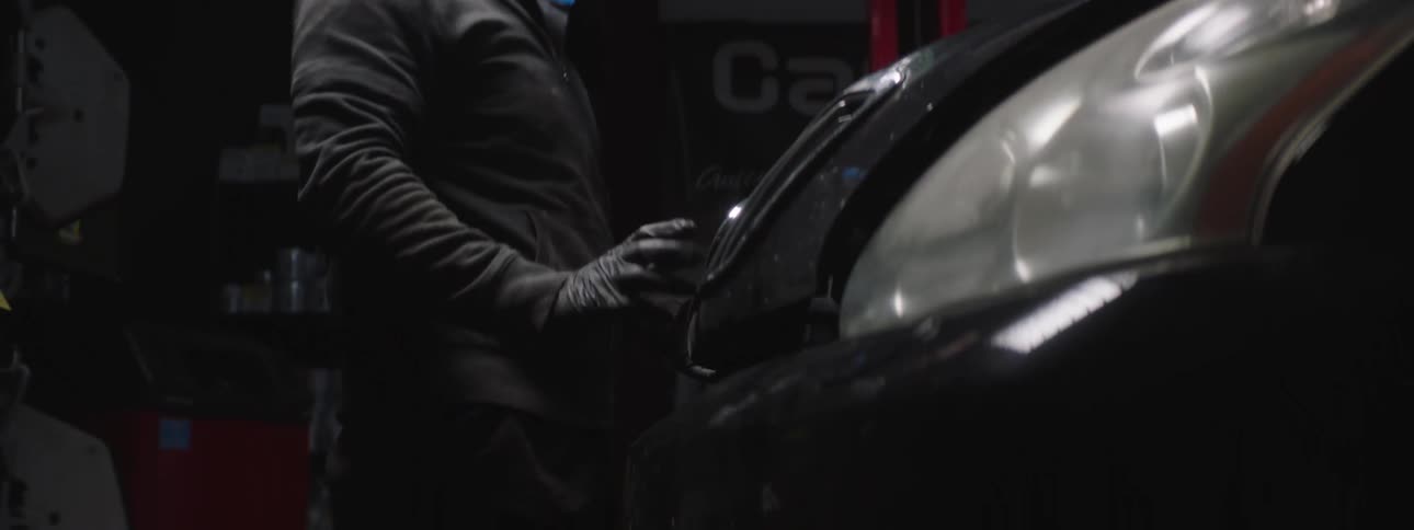 A man shuts the hood of a car in a garage