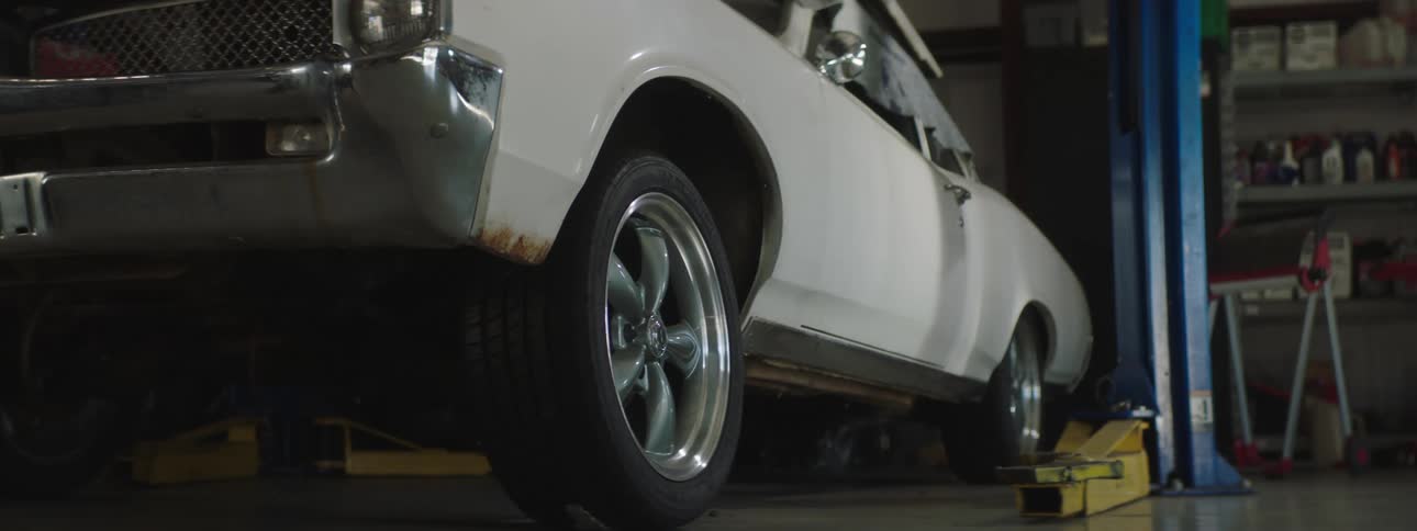 A white vintage muscle car sits in an auto garage