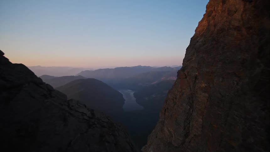 Aerial pushing through mountain canyon at sunset to reveal distant lakes and peaks