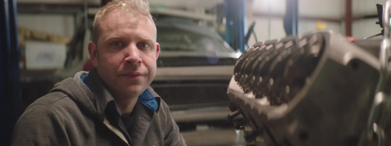 A man is sitting by a vehicle in a car shop