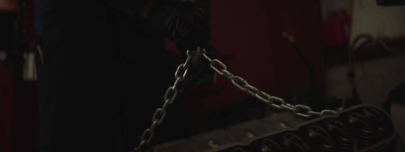 An auto mechanic attaches a chain to an engine in order to hoist it upwards