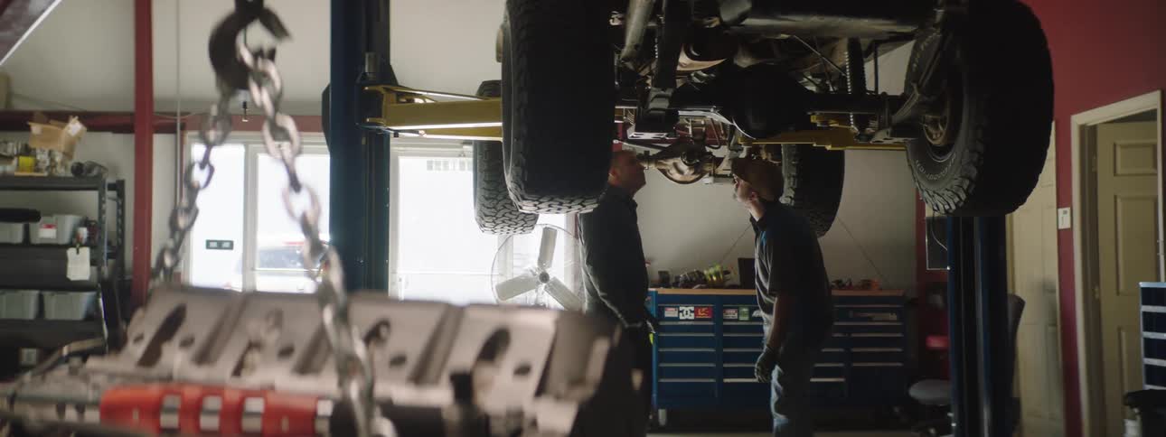 Two car mechanics are working on a car together