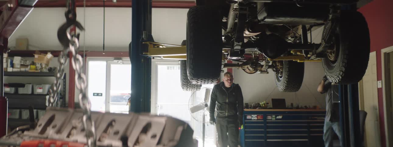 Two mechanics walk under a vehicle to look at it