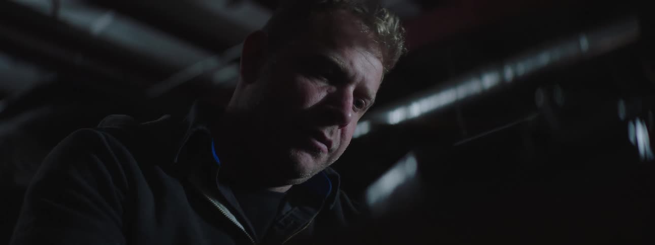 A man in a dark building concentrates as he looks down at an object