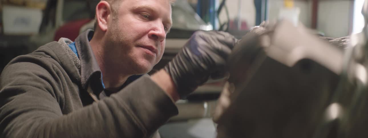 A mechanic wipes an engine with a rag