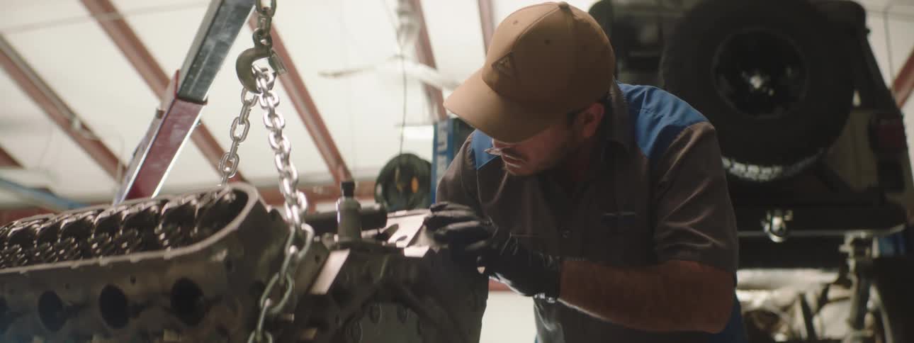 A mechanic looks over a piece of equipment hanging from a chain
