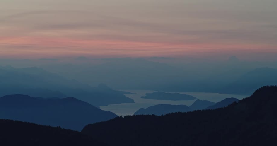 Mountains and lake seen through a haze under a pink dusk sky