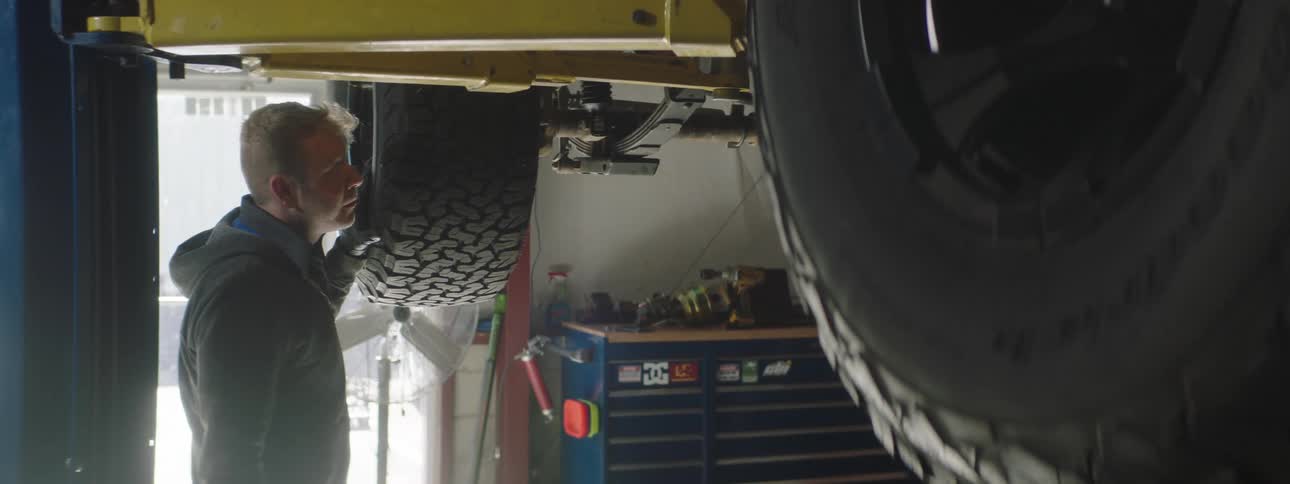 A man stands underneath a vehicle lifted in the air at a commercial garage