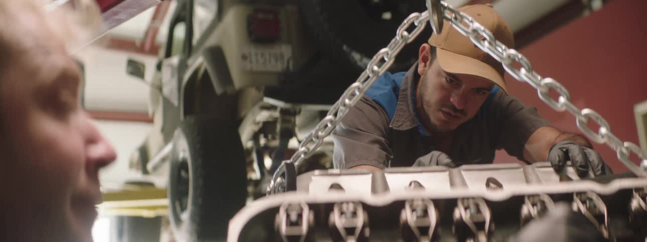 Two men are working on an engine block suspended by a chain
