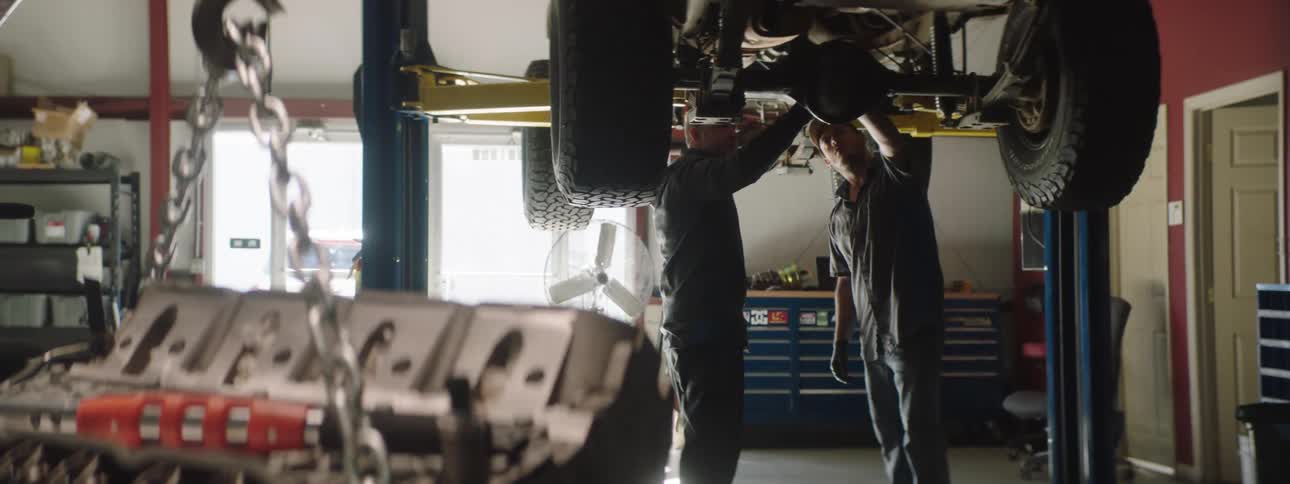 Two auto mechanics inspect the undercarriage of an automobile that is elevate on the lift above them