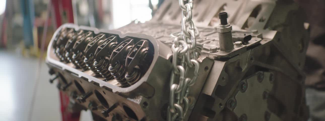 Two mechanics work on a transmission hanging from chains in an auto garage