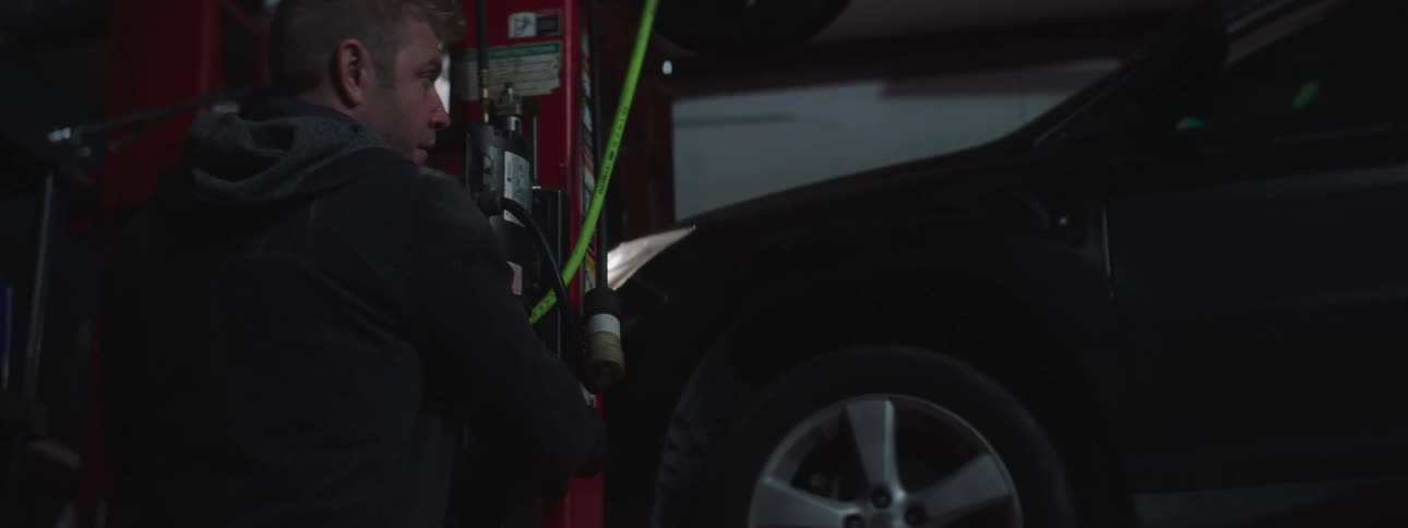 A mechanic lowers a sedan from a riser in an auto garage