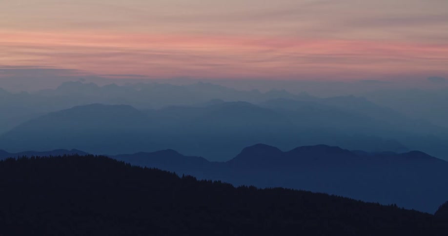 A landscape with silhouette of trees and mountain ranges at dusk