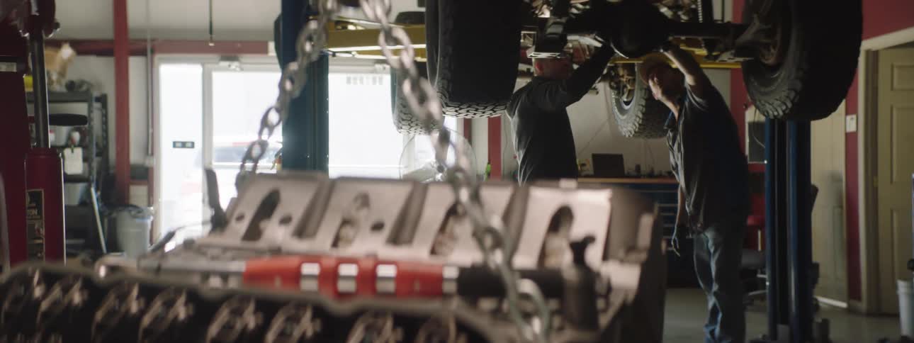 Two auto mechanics inspect the undercarriage of an automobile that is raised on the lift above them