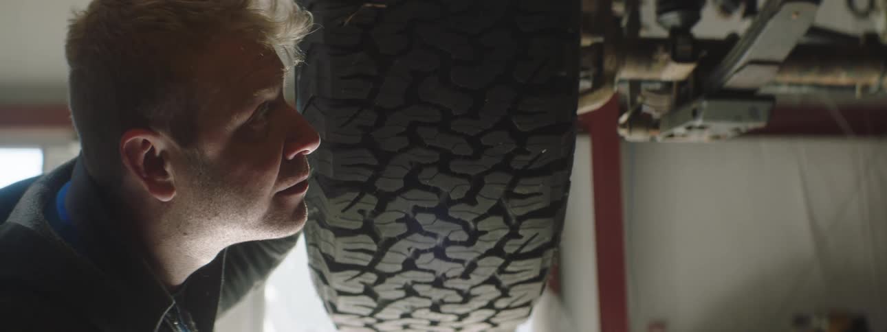 A mechanic examines the bottom of a lifted car in a garage
