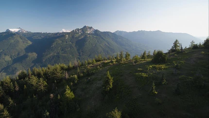 Sweeping aerial of mountain meadow reveals mountain biker climbing trail