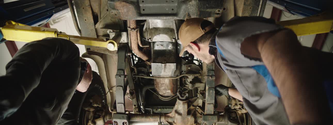 Two people looking at the underside of a car