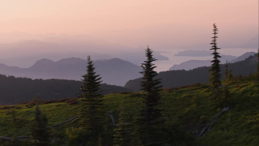 A mountain biker pedals on an exposed ridge at sunset with a vista in the background