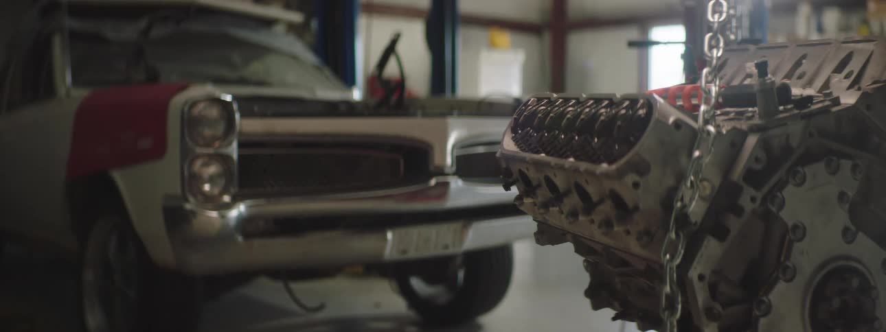 A vehicle transmission hangs from chains near a pickup truck in an auto garage