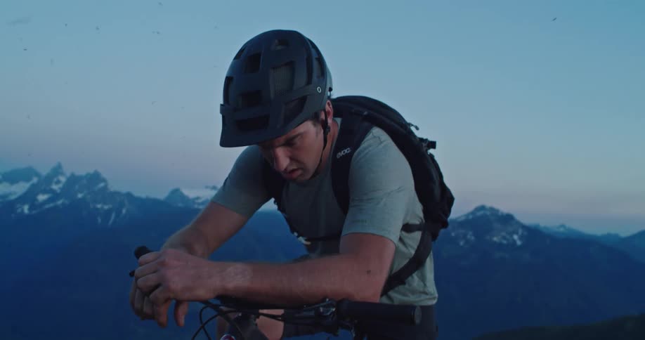 A man looks up from his bike at the summit of a mountain at dusk