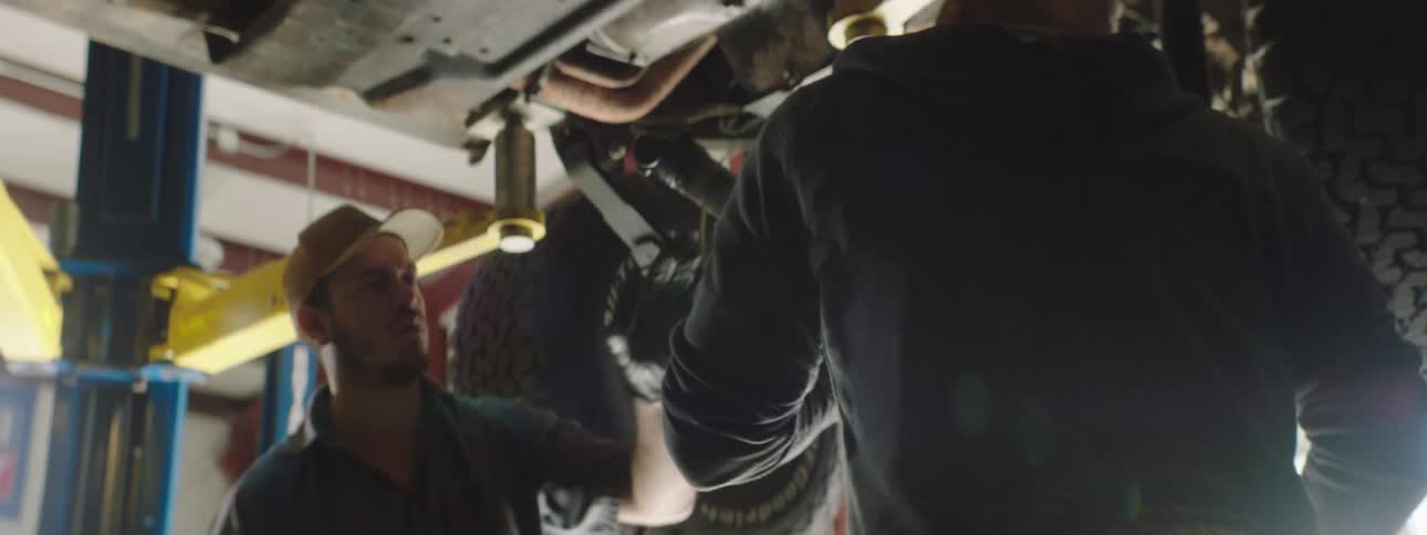 Two mechanics work on the undercarriage of a vehicle in an auto garage