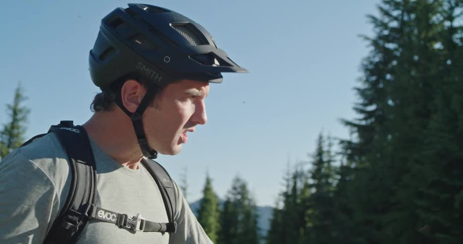 A man standing on a bicycle in a forested mountain area takes a drink from a water bottle