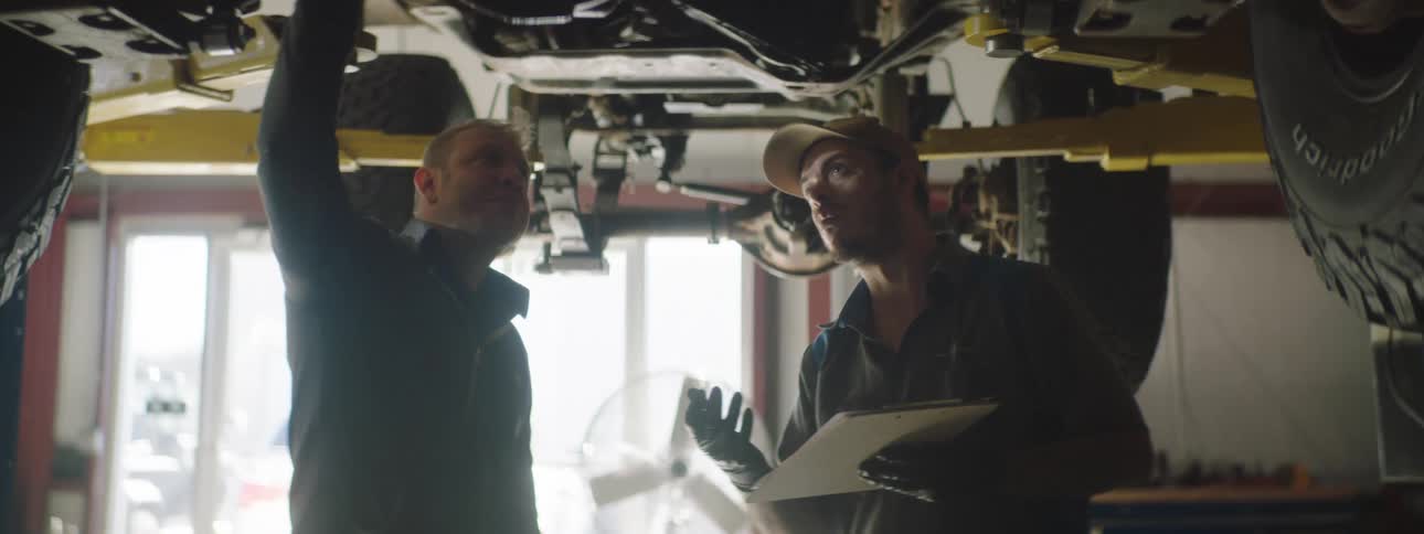 Car mechanics standing under a car check the car parts taking notes at the garage