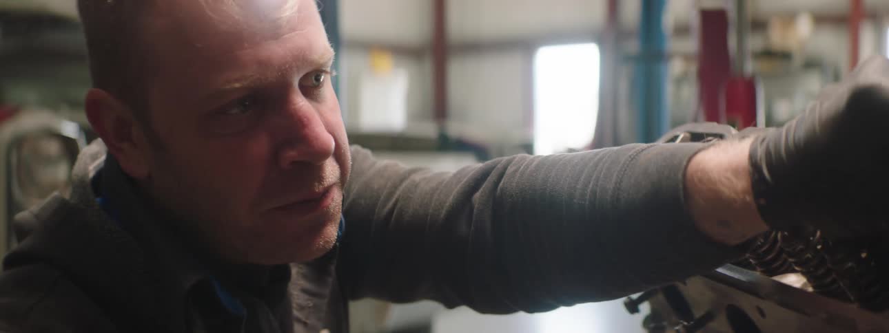 A man with gloves in a garage working with a vehicle a wall and windows in the background