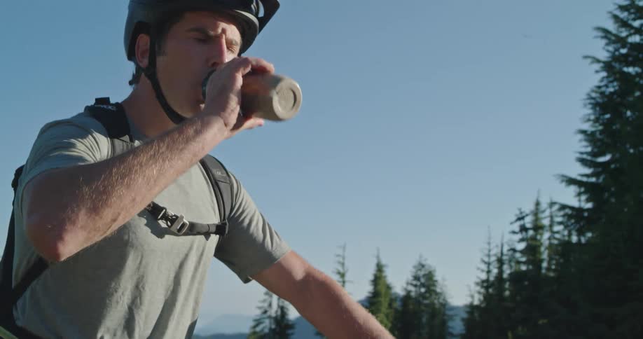 A man sitting on his mountain bike takes a drink from his water bottle on a sunny day