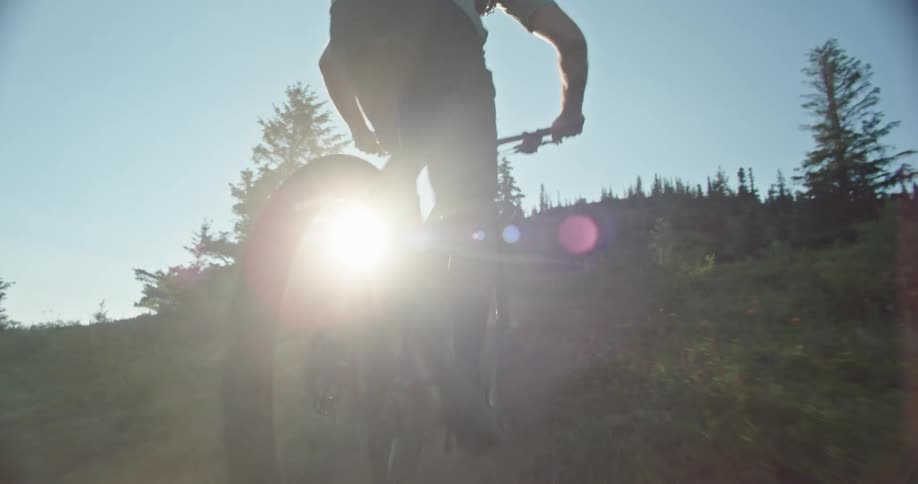 A man climbs a steep mountain bike trail as the sunlight pokes through his wheels